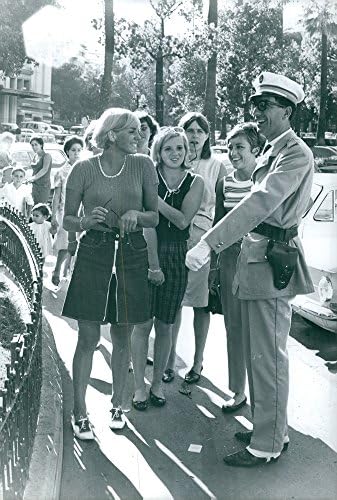 Vintage fotografija Christine Caron sa svojim prijateljima i razgovara sa muškarcem u uniformi.